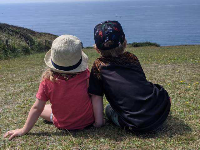 Two children sat looking out over cliffs to the sea