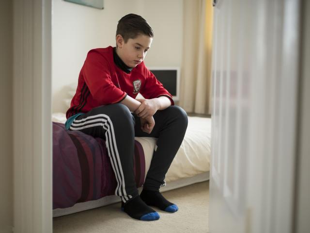 Child who could be vulnerable sitting on bed looking upset