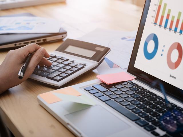 Hand typing on calculator next to laptop showing graphs