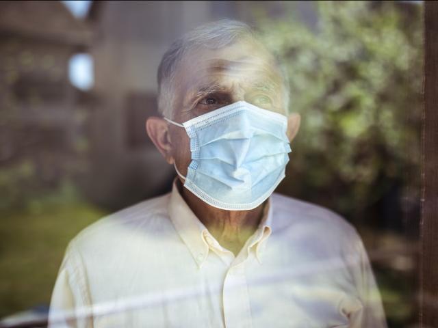 Older man wearing face mask behind window