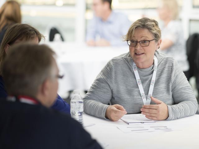 Woman sat at table chatting to a man.