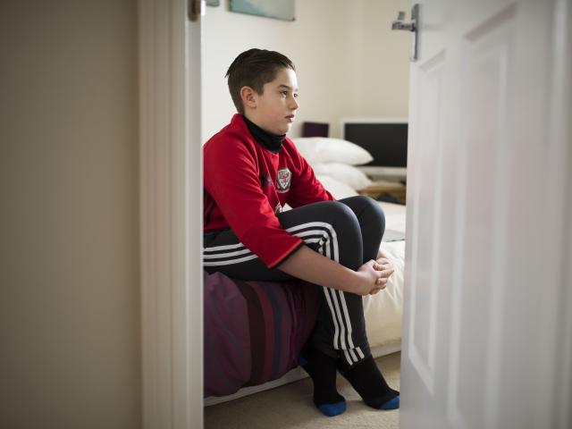 Young boy sat in bedroom looking sad