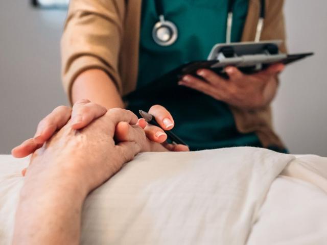 Patient lying down with hands across stomach and member of staff next to them