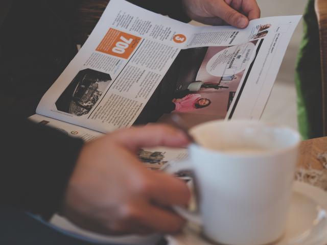 person reading a newspaper with a cup of coffee