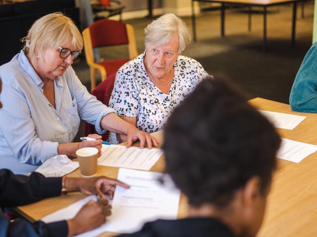 Two women sitting behind the table with documents in front of them.