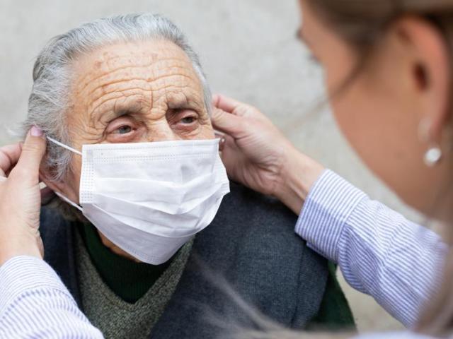 An elderly woman getting her mask put on by a carer.