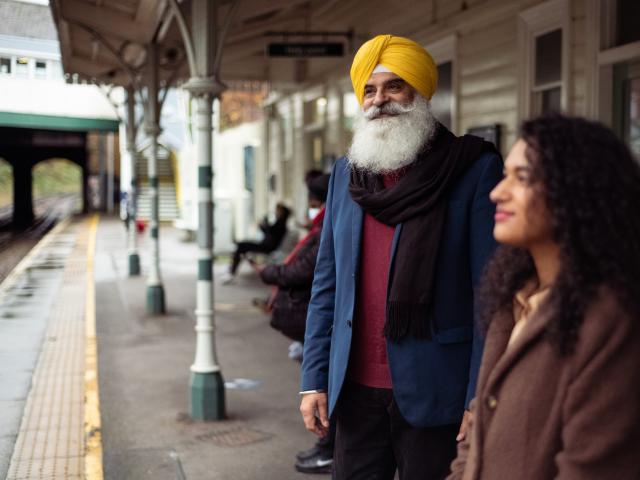 An older gentleman with long beard waiting on a train station. 
