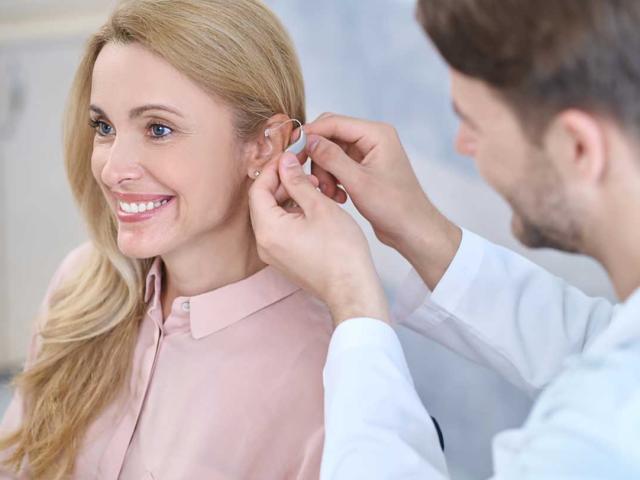 A doctor putting a hearing aid on a woman.