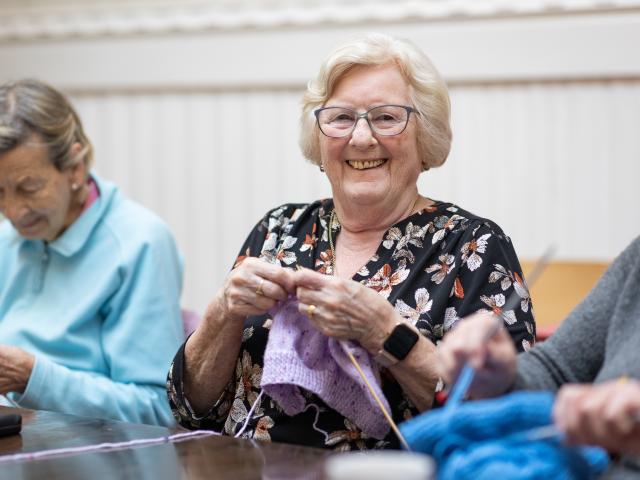 Older woman smiling and knitting
