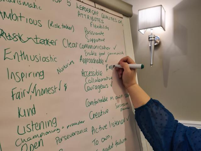 A hand writing a list of leadership qualities on a flip chart