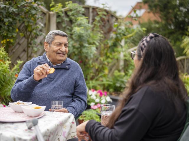 An older Indian man getting served snacks by a woman carer with dark long hair.