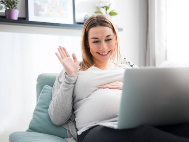 A pregnant woman waving at the laptop. 