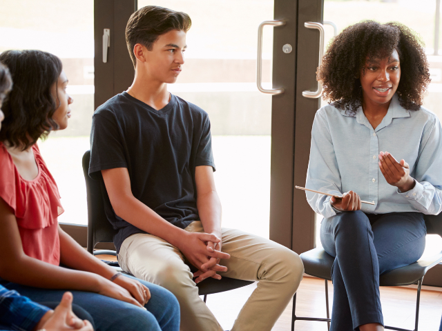 A young black women on the right speaking to group of peers. To her left there is a young boy.