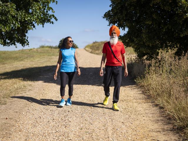 Two people walking on a dirt road. A man on the right is wearing a red t-shirt while the woman on the left is wearing a blue top.