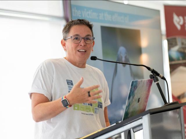 Female speaker in a white t-shirt at a lectern