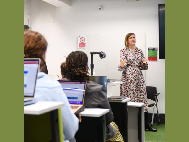 Woman at front of room talking to people with laptops open