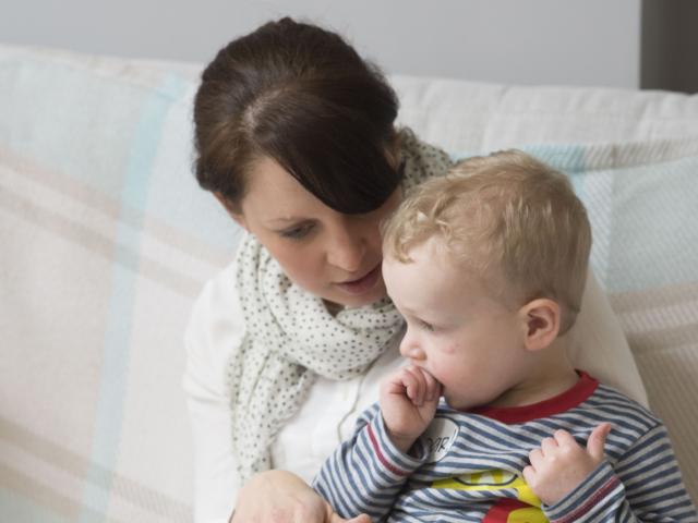 A dark-haired woman holding a baby with blonde hair. 