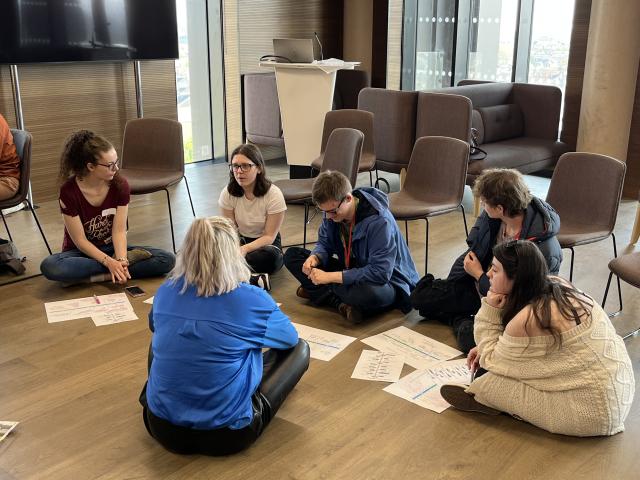 A group of people sitting on the floor in a circle and discussing something. 