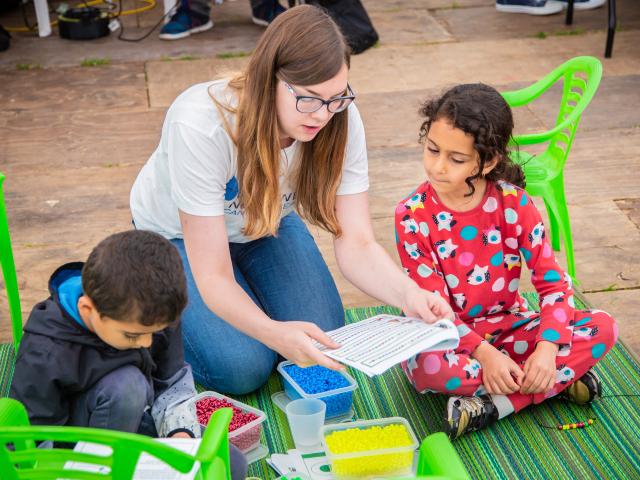 A research sitting on a ground and talking to young children.