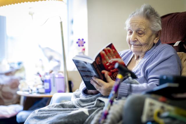 an old woman reading a book on the armchair