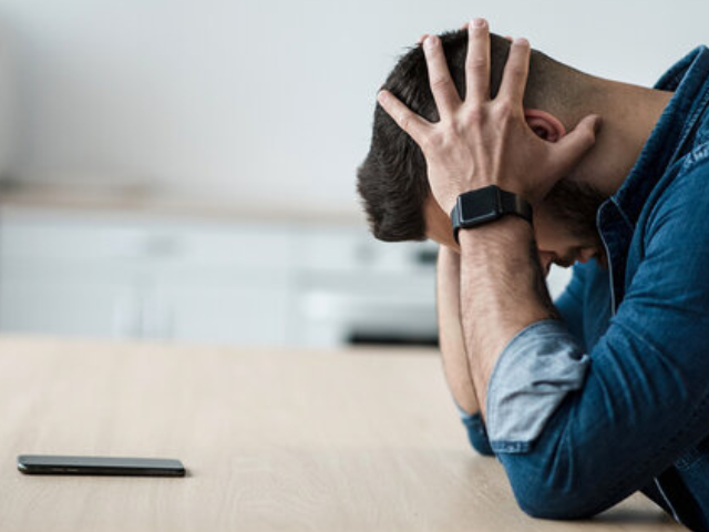 A man wearing a smartwatch sitting at the table with his head in hands. 