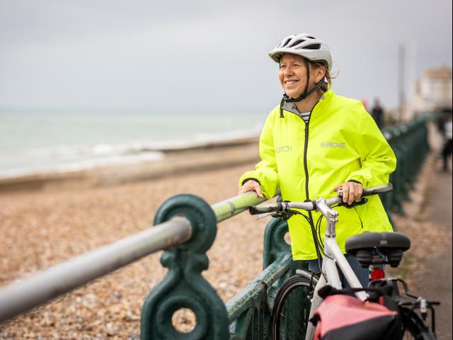 An elderly woman riding a bike on a coastline. 