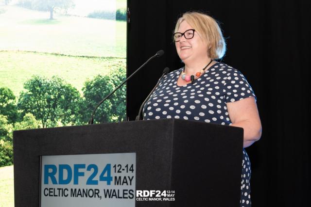 Woman stood on stage at lectern smiling