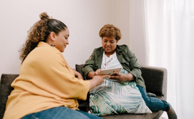 Two women sat on sofa looking at tablet