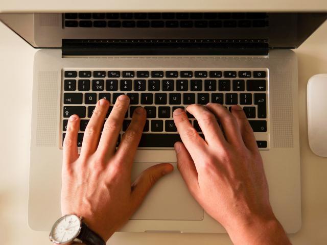 male hands hovering over a laptop keyboard
