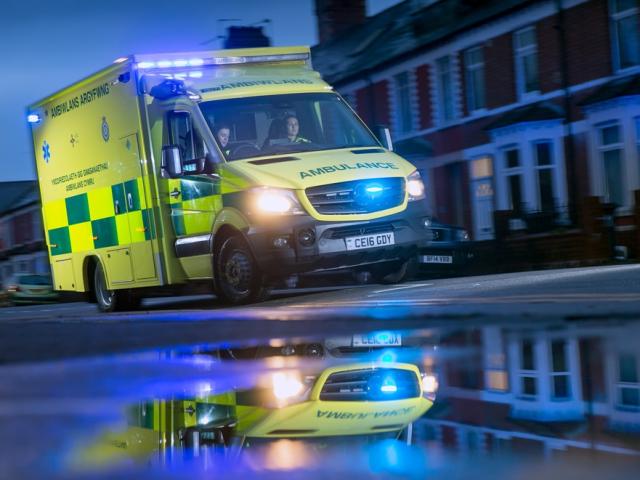 Ambulance driving down wet street with blue lights flashing
