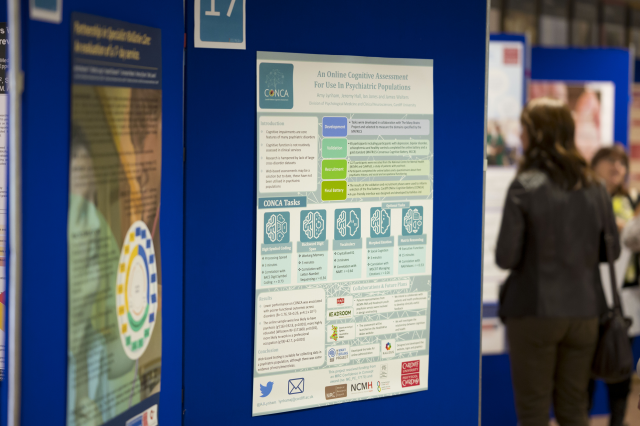 People stand near informational posters displayed on blue boards at a conference.