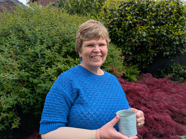 Gwen in her garden holding a cup of coffee