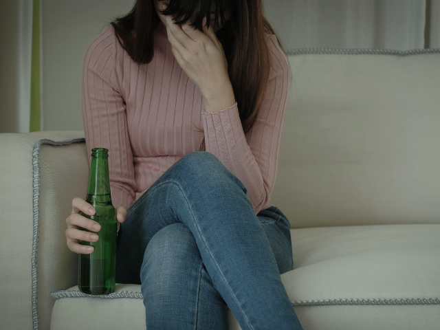 A woman sat on the couch looking down with a bottle in her hand