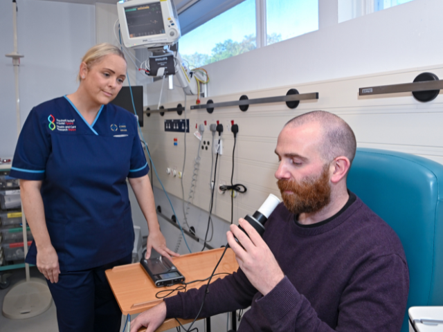 Someone in NHS uniform looking at a patient blowing into a tube