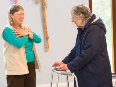 Woman teaching exercise to older woman in care home