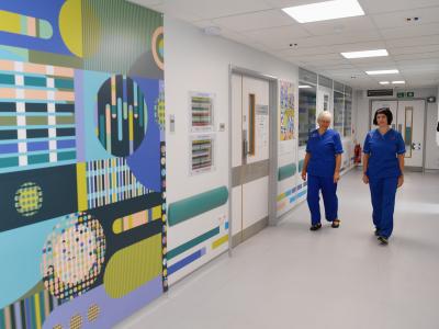 Two female nurses in blue scrubs walking through hospital corridor. 