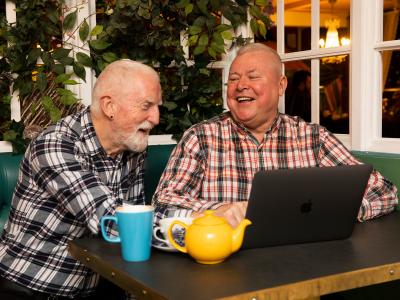 Two old men laughing at memes on a macbook