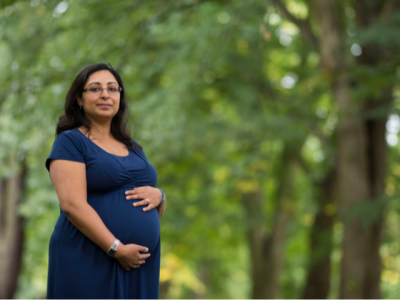 Pregnant woman holding her belly with trees in the background